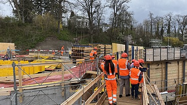 Schulklasse mit Schutzhelmen geht über einen Holzsteg auf einer Baustelle in Kloten.