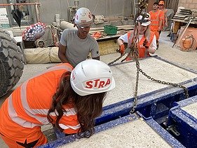 Drei Lernende befestigen dicke Ketten an einem Betonelement