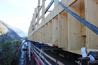 Ein Gerüst und Holzelemente einer STRABAG Baustelle in den Schweizer Bergen bei schönem Wetter.