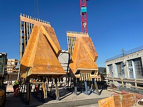  Ein Kran der STRABAG hebt nachts ein langes Brückenteil über Bahngleise. Die Baustelle ist hell erleuchtet.