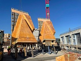  Ein Kran der STRABAG hebt nachts ein langes Brückenteil über Bahngleise. Die Baustelle ist hell erleuchtet.