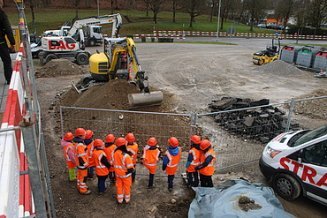 Schulkinder mit Schutzhelmen und Westen probieren auf einer Baustelle in Kloten einen Bagger aus.