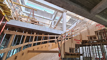 Zwei grosse Hebevorrichtungen auf einer STRABAG-Baustelle. Im Hintergrund sind Bauarbeiter:innen und ein Kran zu sehen.