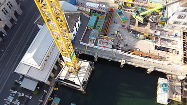 Vogelperspektive hinunter auf die Baustelle und den Fluss.