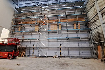 Wand mit Gerüst vom Boden bis zur Decke und eine rote Hebebühne davor