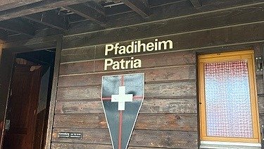 Blick auf die Holzfassade des Pfadiheims an der gerade ein Lernender dabei ist die neuen Holz Latten für die Fassade zusammenzustecken