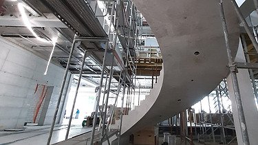  Ein Kran der STRABAG hebt nachts ein langes Brückenteil über Bahngleise. Die Baustelle ist hell erleuchtet.