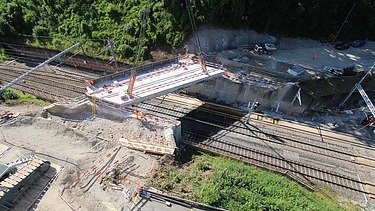 Eine Bahngleisüberquerung, die von einem Kran eingehoben wird. Im Hintergrund ist ein dichter Wald.