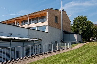 Aufstockung Labor von ETH Zürich - STRABAG Holzbau Modernes Laborgebäude der ETH Zürich mit Holzfassade und Metallverkleidung, umgeben von gepflegtem Rasen und Bäumen bei blauem Himmel.