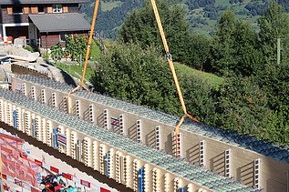 Zwei grosse Holzträger liegen nebeneinander auf der Konstruktion, während der Kran im Hintergrund seine Seile wieder löst.