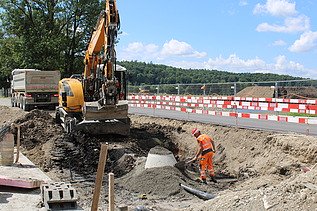 Foto von Arbeiten an einer Baugrube ein Bauarbeiter in Orange und ein Bagger