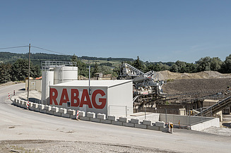 Industriegelände eines Kieswerks, umgeben von Kies- und Sandhaufen unter klarem Himmel.