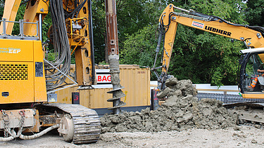 Der Bohrer schüttelt Aushubmaterial ab, mit Bagger wird das Material sofort abtransportiert.