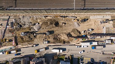 Rüschlikon Bahnhof Süd – STRABAG Tiefbau und Spezialtiefbau Drohnenaufnahme der Baugrube von oben, zu sehen sind mehrere Bagger, die Bahnlinie welche parallel zur Baugrube verläuft sowie Baustellenfahrzeuge