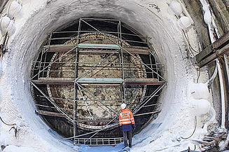 In der Mitte einer Bodenvereisung steht ein Bauarbeiter in Schutzkleidung  vor einem Metallgerüst.