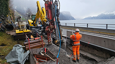 Nahaufnahme mit schwerem Gerät und Mitarbeitern, im Hintergrund der Vierwaldstättersee