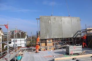 Foto von zwei Baustellenarbeiter die eine Wand einsetzen mit Hilfe eines Krans