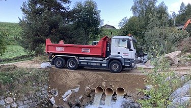Abtransport - STRABAG Ingenieurbau Ein Lastwagen der STRABAG steht am Aclettbach bei Disentis für den Abtransport bereit. Darunter sieht man Durchlaufrohre mit laufendem Wasser.