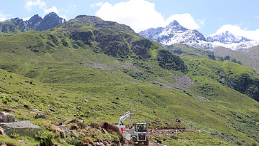 Weisse STRABAG Baumaschinen, im Hintergrund Berglandschaft