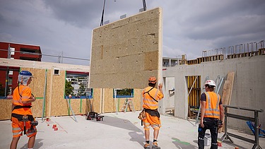 Foto von Holzbauarbeiten mit Kran und Bauarbeiter:innen