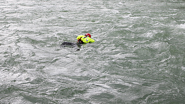 Eine Person schwimmt mit einer automatisch ausgelösten Rettungsweste in der Strömung eines Flusses während einer Wasserrettungsübung.