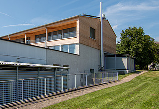 Modernes Laborgebäude der ETH Zürich mit Holzfassade und Metallverkleidung, umgeben von gepflegtem Rasen und Bäumen bei blauem Himmel.