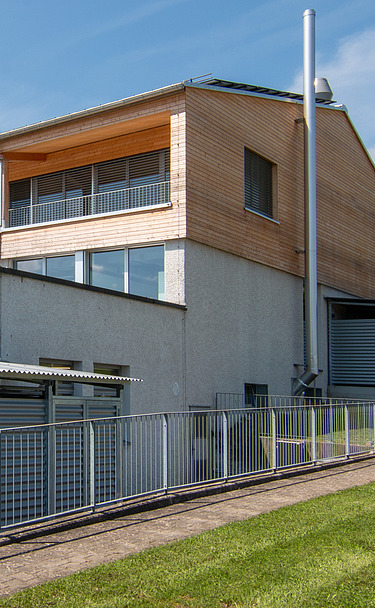 Aufstockung Labor von ETH Zürich - STRABAG Holzbau Modernes Laborgebäude der ETH Zürich mit Holzfassade und Metallverkleidung, umgeben von gepflegtem Rasen und Bäumen bei blauem Himmel.