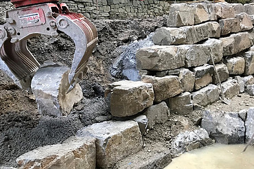 Bauarbeiten in Wädenswil - STRABAG Tiefbau Foto von einer Krangreifer der einen Stein zu einer Mauer hebt