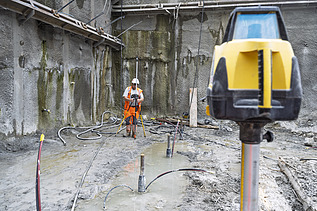 Ein Bauarbeiter ist in der Baugrube beim Vermessen mit Laser, im Vordergrund das Lasergerät im Hintergrund er