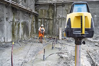 Ein Bauarbeiter ist in der Baugrube beim Vermessen mit Laser, im Vordergrund das Lasergerät im Hintergrund er