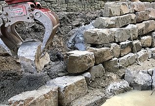 Foto von einer Krangreifer der einen Stein zu einer Mauer hebt