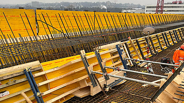  Ein Kran der STRABAG hebt nachts ein langes Brückenteil über Bahngleise. Die Baustelle ist hell erleuchtet.