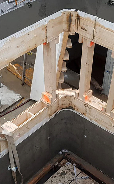 Nachtaufnahme einer STRABAG-Baustelle. Ein grosser Kran steht beleuchtet neben einem Wohnhaus unter dem klaren Nachthimmel.