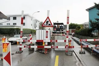 Baustelle in der Amriswilerstrasse mit rot-weissen Absperrungen der STRABAG AG, einem Bagger im Hintergrund, Werkleitungen entlang des Gehwegs und einem vorbeifahrenden Auto auf der linken Seite.