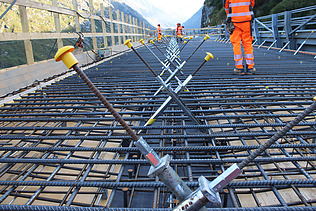 Bauarbeiter:innen stehen auf einer Bewehrung aus Stahlmatten, um Beton für eine neue Brücke in den Bergen zu giessen.