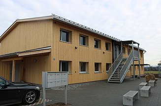 Asylunterkunft aus Holz, zweistöckig mit Metalltreppe und Geländer. 