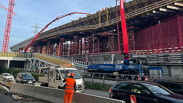 Zwei grosse Hebevorrichtungen auf einer STRABAG-Baustelle. Im Hintergrund sind Bauarbeiter:innen und ein Kran zu sehen.