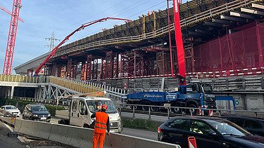 Zwei grosse Hebevorrichtungen auf einer STRABAG-Baustelle. Im Hintergrund sind Bauarbeiter:innen und ein Kran zu sehen.