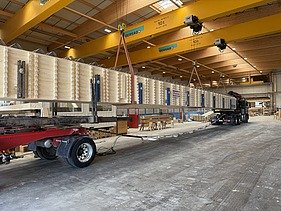 Verladen eines Holzträgers auf einen Lastwagen in einer Halle.