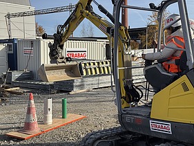Ein Schüler sitzt im kleinen Bagger und probiert unter Anleitung auf der Baustelle erste Steuerbewegungen aus.