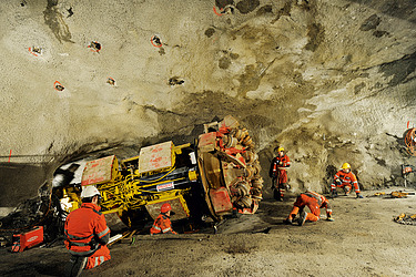 Arbeiter mit orangefarbener Kleidung arbeiten in einem grossen Fels­tunnel.