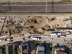 Rüschlikon Bahnhof Süd – STRABAG Tiefbau und Spezialtiefbau Drohnenaufnahme der Baugrube von oben, zu sehen sind mehrere Bagger, die Bahnlinie welche parallel zur Baugrube verläuft sowie Baustellenfahrzeuge