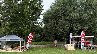 Zwei STRABAG Stände mit Zelten und Infomaterial auf einer grünen Wiese unter Bäumen.