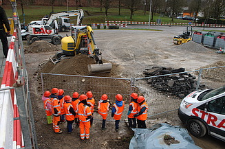 Schulkinder mit Schutzhelmen und Westen probieren auf einer Baustelle in Kloten einen Bagger aus.