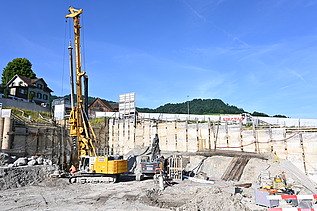Ein grosser 15m hoher Bohrer in einer Baugrube bei der Arbeit. Im Hintergrund sieht man einen strahlend blauen Himmel. 