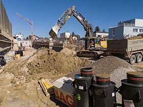 Rüschlikon Bahnhof Süd – STRABAG Tiefbau und Spezialtiefbau Bagger hebt Loch aus. Daneben ein LKW wo den Aushub abtransportiert