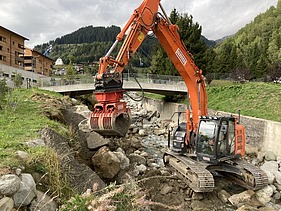 Arbeiten im Bach - STRABAG Ingenieurbau Bagger der STRABAG arbeitet an einer Flussverbauung am Aclettbach bei Disentis. Eine Brücke führt über den Bach.