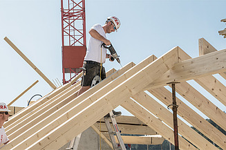 Zwei STRABAG - Mitarbeiter arbeiten im Holzbau an der Dachkonstruktion eines Gebäudes.