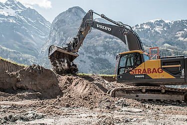 STRABAG - Bagger führt Erdarbeiten in einer bergigen Landschaft durch.