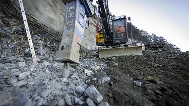 Bagger spitzt den Fels auf, im Vordergrund Geröll